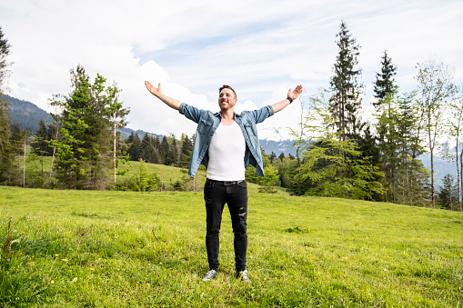 Handsome man is standing in the mountains with his arms wide open. Concept: back to nature, simple life