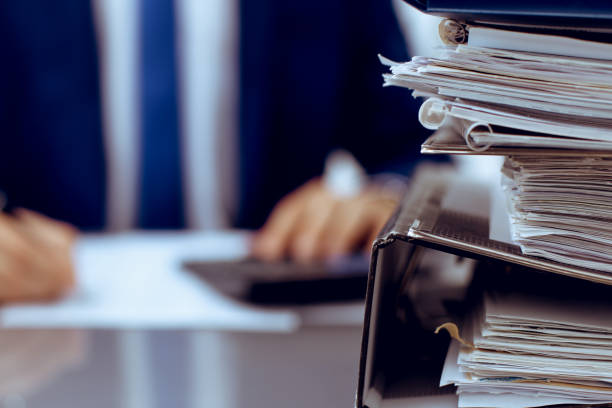 istock Binders with papers are waiting to be processed with businessman back in blur. Accounting planning budget, audit, insurance  and business concept 1159979259