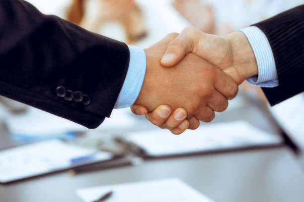 istock Business people shaking hands at meeting while theirs colleagues clapping and applausing. Group of unknown businessmen and women in modern white office. Success teamwork, partnership and handshake concept. 1159979295
