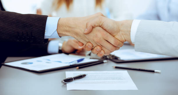 istock Business people shaking hands at meeting while theirs colleagues clapping and applausing. Group of unknown businessmen and women in modern white office. Success teamwork, partnership and handshake concept. 1159979327