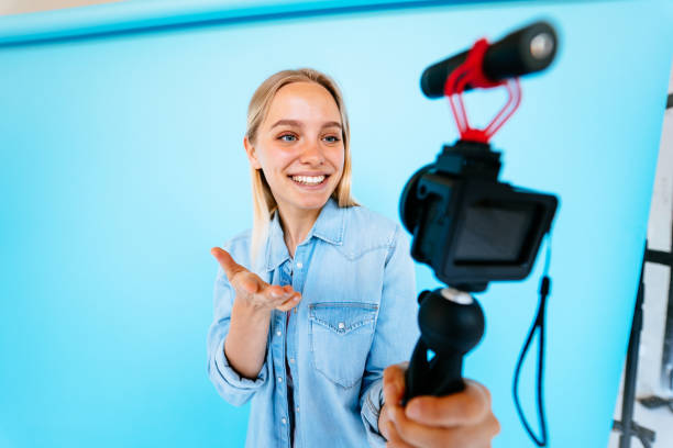 Beautiful girl blogger relieves itself at camera isolated blue background Beautiful girl vlogger relieves itself at camera isolated over blue background in studio relieves stock pictures, royalty-free photos & images