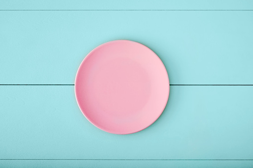 Pink empty plate on turquoise wooden table. Top down view with copy space.