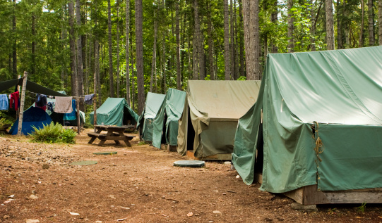 A typical campsite at a Boy Scout Camp includes tents, a table, dirt, and dirty clothes drying on a rope.