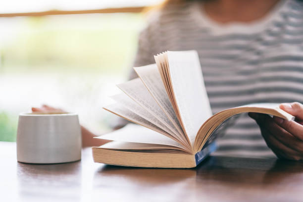 istock a woman holding and reading a book while drinking coffee 1159985514