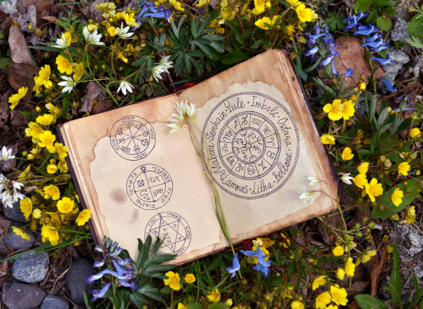 Open book with wiccan festivals chart among spring flowers. stock photo