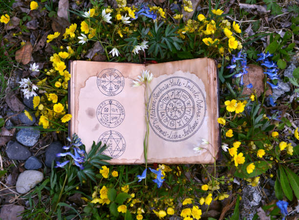 istock Open book with wiccan festivals and magic charts in grass and flowers. 1159985641