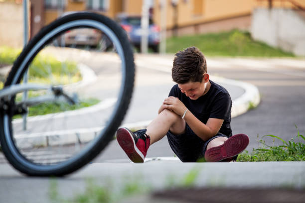 boy in the street ground with a knee injury screaming after falling off to his bicycle. kid hurts his leg after falling off his bike - child bicycle cycling danger imagens e fotografias de stock