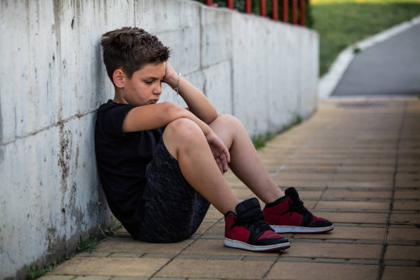istock Boy sitting and thinking about something sad. Isolation and bullying concept. Kid sad and unhappy, child was crying, upset, feel sick 1159987972