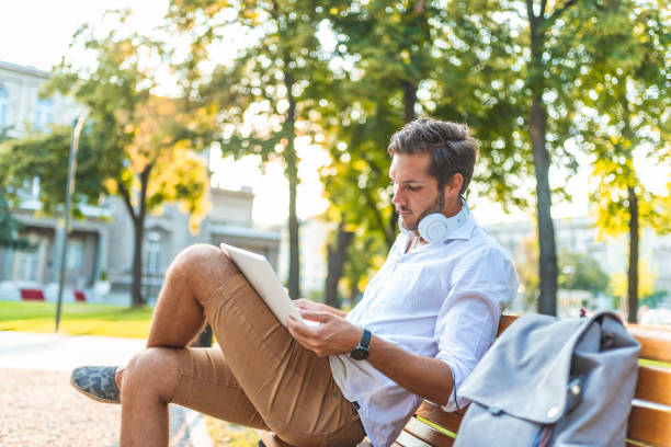 istock Happy man sitting on bench and using laptop in a park 1159988298