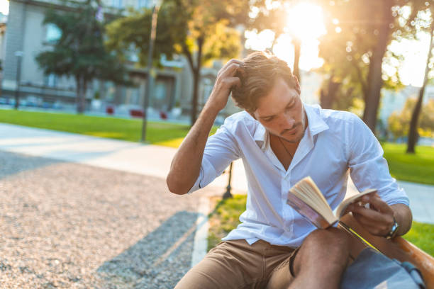 istock Handsome man reading book outdoors 1159988319