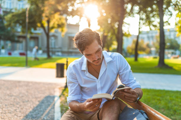 istock Handsome man reading book outdoors 1159988911
