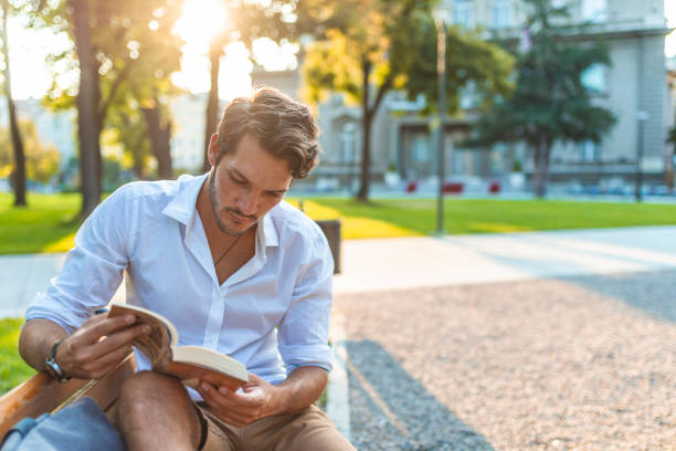 istock Guy sitting on a bench in the park reading book 1159989092