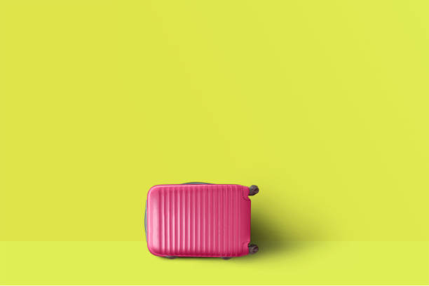 Pink suitcase next to the yellow pastel color wall. Concept of tourism and traveling