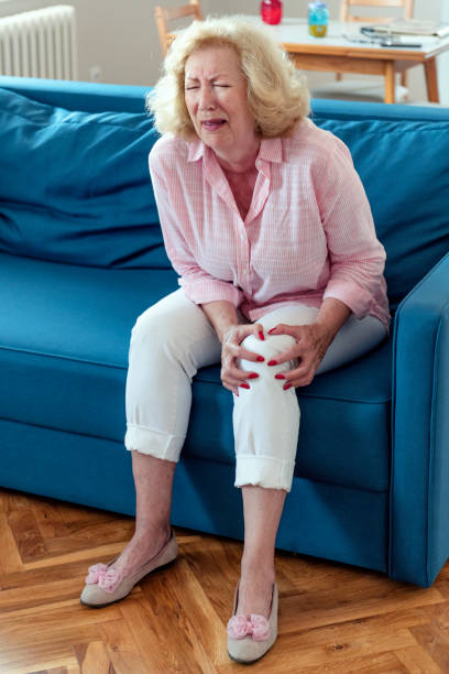 소파에 앉아 다리와 무릎 부상에 통증으로 고통 노인 여성. - arthritis senior adult rheumatoid arthritis sadness 뉴스 사진 이미지