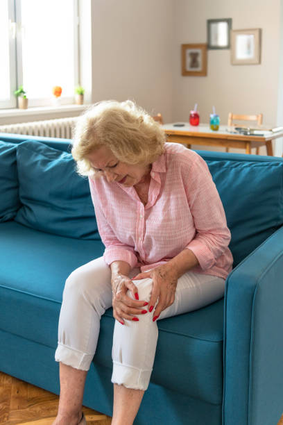 starsza kobieta cierpiąca na ból nóg i uraz kolana siedząca na kanapie. - arthritis senior adult rheumatoid arthritis sadness zdjęcia i obrazy z banku zdjęć