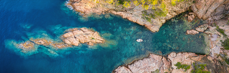 Panoramic aerial top view of a boat in the water surface in front of a little beach