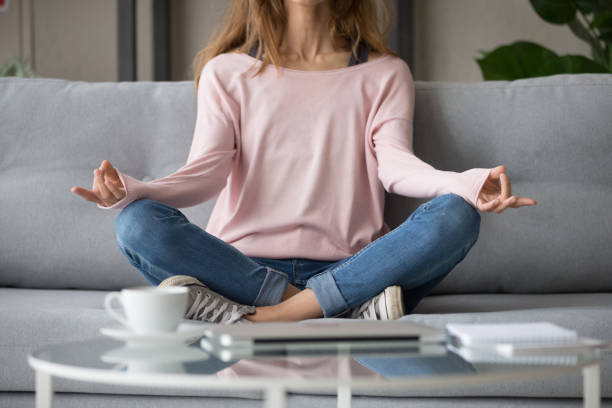 istock Cropped image woman sitting on couch in lotus pose meditating 1159994002
