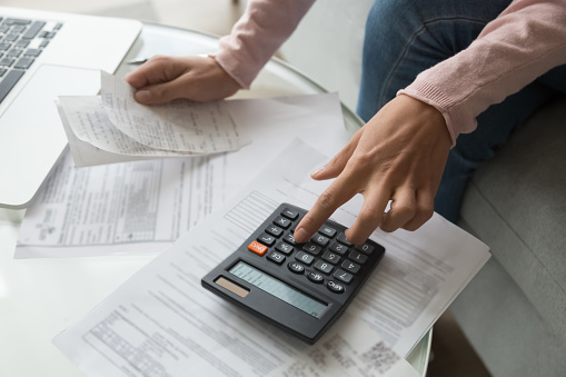 Close up cropped image coffee table full with papers invoices cheque bills, female hands holding receipt calculating company expenses results of incomes, bookkeeper accountant doing paperwork concept