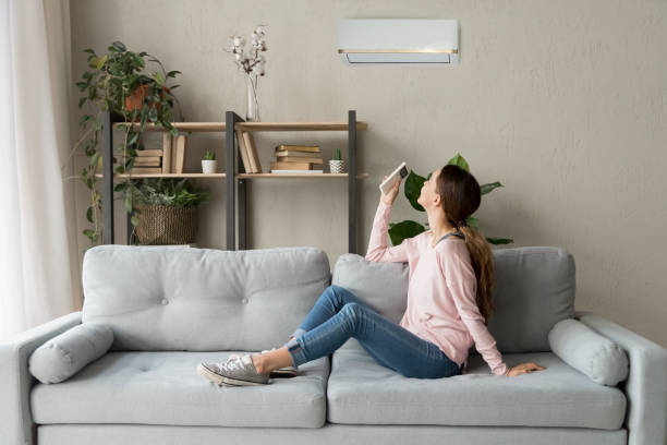 Happy woman holding cooler system remote controller enjoy fresh air Happy woman rests on couch in modern cozy living room looks up on wall holds cooler system remote controller air conditioner user enjoy fresh air in hot summer day, set comfortable temperature indoors adjusting seat stock pictures, royalty-free photos & images