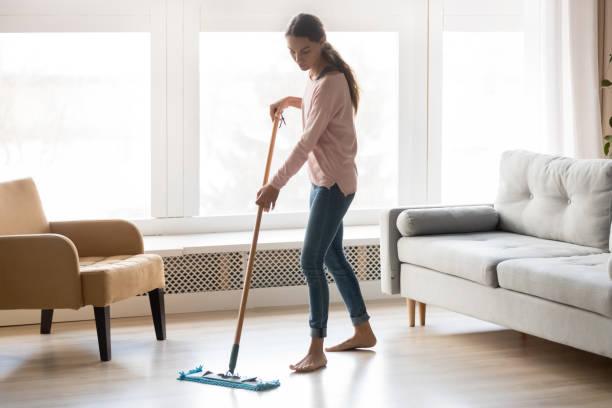 Barefoot girl doing house cleaning using microfiber wet mop pad Full-length image of barefoot young woman stands in living room homeowner doing house chores cleaning wooden laminate floor using microfiber wet mop pad, housekeeping job or routine home work concept mop photos stock pictures, royalty-free photos & images