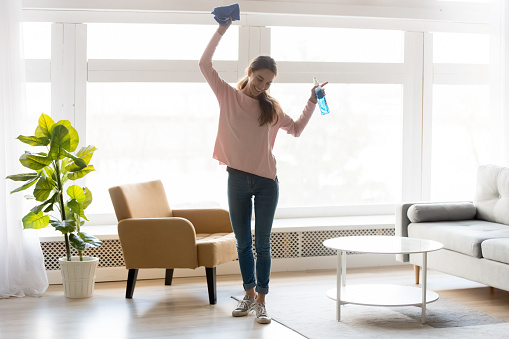 Full-length woman in casual clothes dance do house cleaning holds blue rag spray bottle detergent feels happy, qualified housekeeping specialist agency hiring, quick fast and easy home chores concept