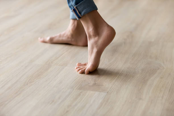 les pieds de femme de vue de plan rapproché de côté se tiennent sur le plancher en bois chaud - pieds nus photos et images de collection