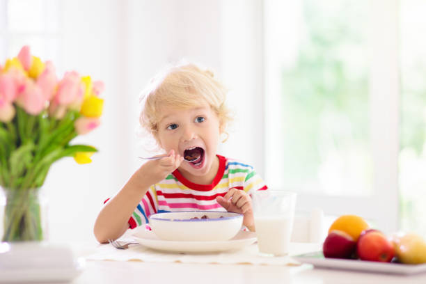 Child eating breakfast. Kid with milk and cereal. Child having breakfast. Kid drinking milk and eating cereal with fruit. Little boy at white dining table in kitchen at window. Kids eat on sunny morning. Healthy balanced nutrition for young kids. boys bowl haircut stock pictures, royalty-free photos & images