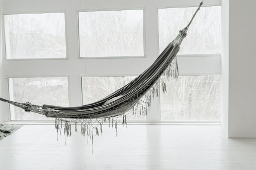 Grey Cozy Hammock in White Minimal Living Room. Lounge Room with Big Window Scandinavian Style Decor. Brazilian Hanging Textile in Loft Boho Apartment. Relax Bedroom Details