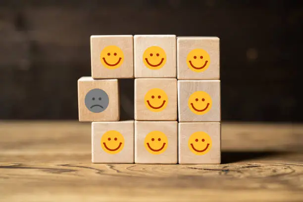 Single unhappy block and group of happy blocks symbolizing feeling lonely on wooden background