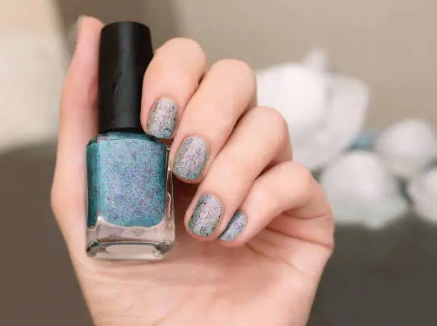 Photo of Female hand with thermal blue nail design holding nail polish bottle.