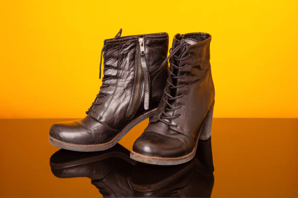 istock Black half boots with high heel on black glass table and yellow background. 1160001890