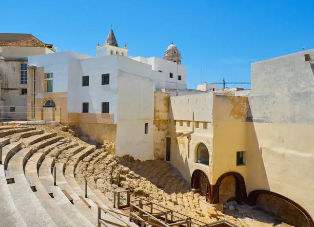 Remains of the Roman Theatre of the ancient Gades in Hispania, with the belfry of the Santa Cruz Cathedral in the background, in the current city of Cadiz, Andalusia, Spain.