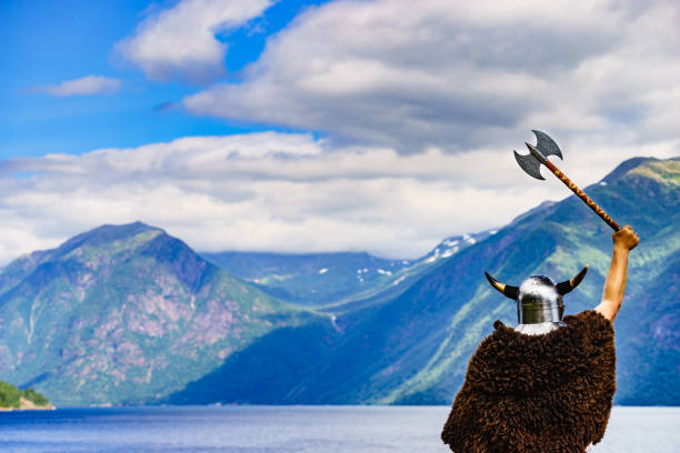 Viking warrior with helmet and axe on fjord shore in Norway. Tourism and traveling concept