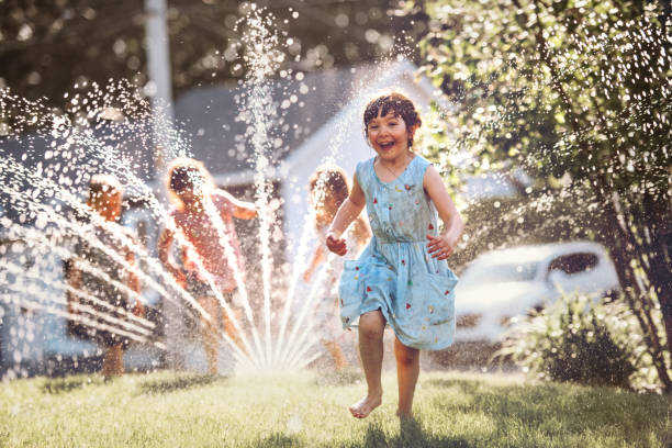 Happy kids playing with garden sprinkler stock photo