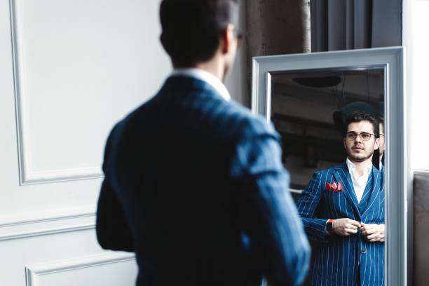istock Perfect look. Reflection of handsome young man in full suit adjusting his jacket while standing in front of the mirror indoors. 1160011960