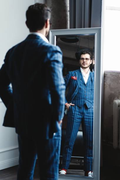 istock Perfect look. Reflection of handsome young man in full suit adjusting his jacket while standing in front of the mirror indoors. 1160011961