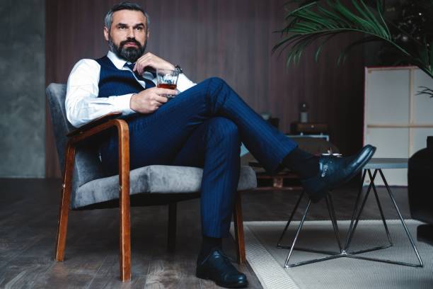 istock Handsome pensive man is touching his beard, looking away and thinking while sitting in armchair indoors. 1160012521