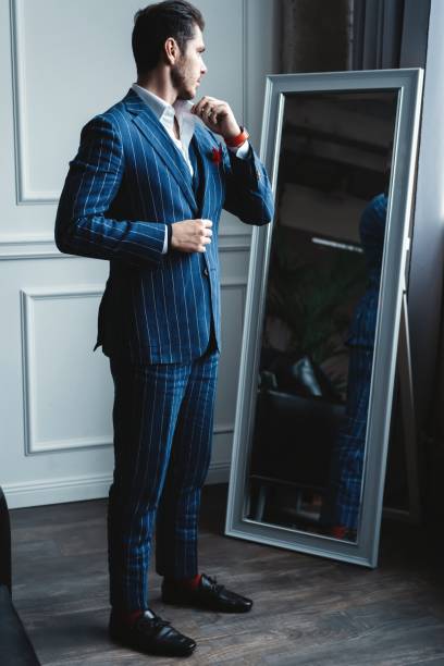 istock Perfect look. Reflection of handsome young man in full suit adjusting his jacket while standing in front of the mirror indoors. 1160012711