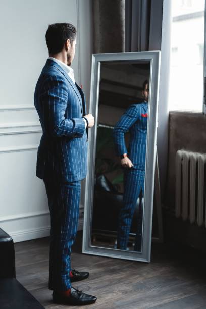istock Perfect look. Reflection of handsome young man in full suit adjusting his jacket while standing in front of the mirror indoors. 1160012713