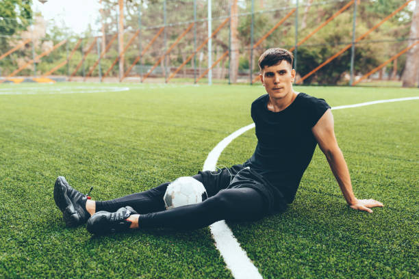 istock Handsome young soccer player man taking a rest after training session outdoors. Healthy and fit man sitting and relaxing at green lawn after workout exercises. People and sport concept 1160012726