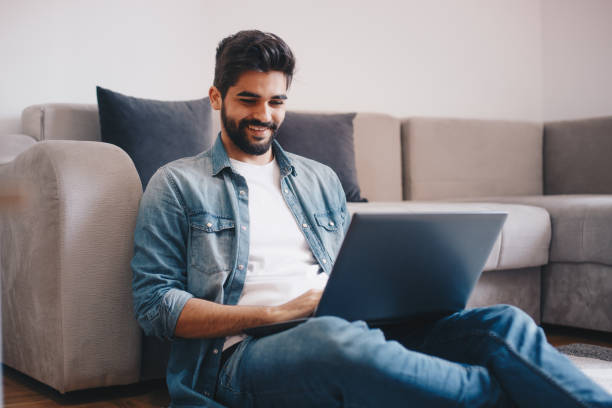 istock Young relaxed man working on laptop while sitting on floor at home 1160013459