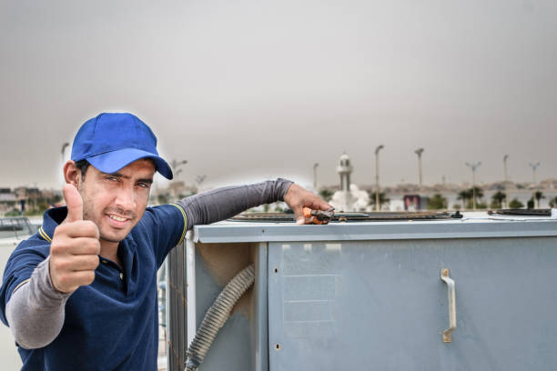 a professional electrician man is giving up thumbs up after the fixing a heavy duty air conditioner on the roof top and wearing blue uniform and cap and the city is in the background un hombre electricista profesional está renunciando a los pulgares hacia arriba después de la fijación de un aire acondicionado de servicio pesado en la parte superior del techo y el uso de uniforme azul y gorra y la ciudad está en el fondo