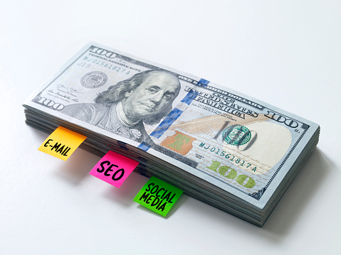 Adhesive notes inside a  pile of 100 dollar bills symbolizing Social media expenses