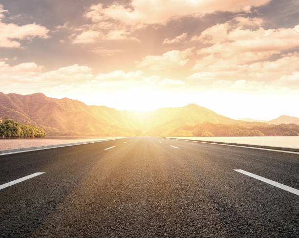 at sunset, the sun shines on a tarmac road stretching from the lake to the distant mountains, joining the mountains. - car horizon over land driving street imagens e fotografias de stock