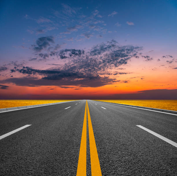 al atardecer, la luz del sol en los pastizales converge con el horizonte en una carretera asfaltada que se extiende hasta las montañas distantes. - car horizon over land driving street fotografías e imágenes de stock