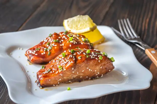 Two pieces of teriyaki salmon garnished with sesame seeds and spring onion