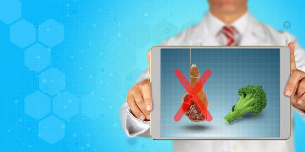 Doctor is holding a digital tablet and showing eat vegetable don't eat meat message on screen A doctor holds a digital tablet and shows eat broccoli don't eat processed meat message on screen in front of blue, hexagonal and technological background. With copy space. dont eat meat stock pictures, royalty-free photos & images