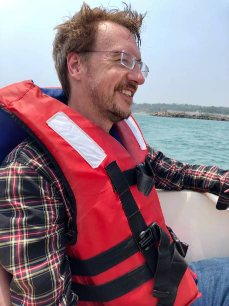 a imagem do homem maduro sentou o sorriso e windvarrido, desgastando um revestimento de vida em um lancha que viaja na velocidade fora da costa da praia de kovalam, kerala, india - life jacket equipment safety jacket - fotografias e filmes do acervo