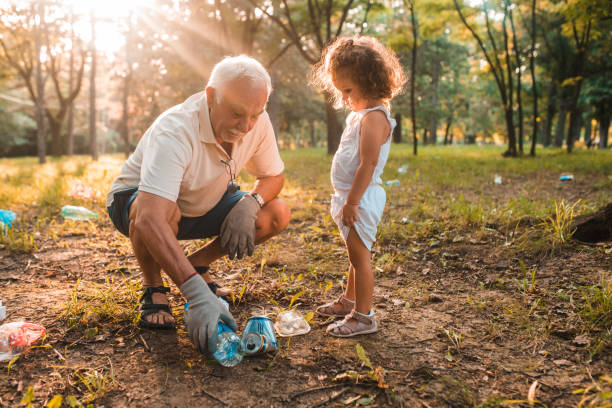 Grandfather and granddaughter recycling Grandfather and granddaughter picking up water bottles and recycling recycling bin photos stock pictures, royalty-free photos & images