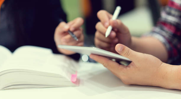istock close up student man hand holding tablet and using stylus pen for asking or consulting about project with professor opening book for help to recommend or suggest at table , educational concept 1160029788